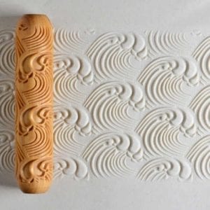Clay texture roller with wave patterns pressed into clay, demonstrating ceramic decoration techniques for pottery.