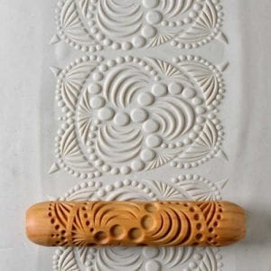 Wooden rolling pin with intricate texture patterns on white clay slab, perfect for ceramic decorating techniques.
