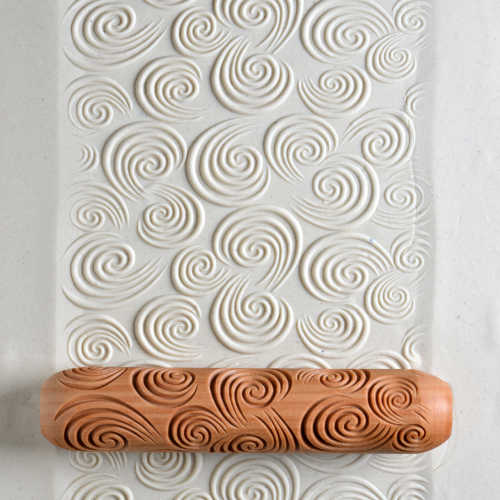 Embossed white clay sheet with swirling patterns rolled with a decorative shaping rolling pin for texture in pottery.