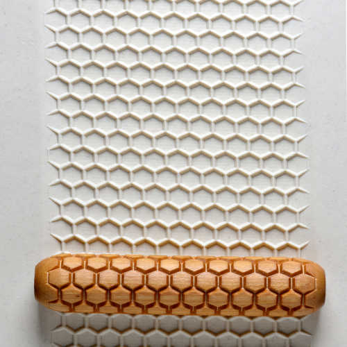 A textured rolling pin with a hexagonal pattern pressed into white clay, ideal for ceramic decorating techniques.