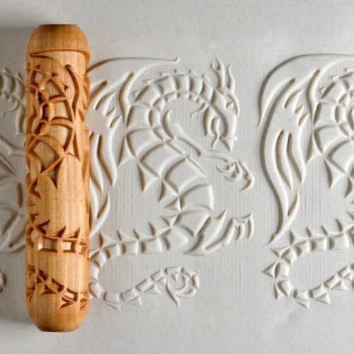 Decorative roller with dragon motifs pressed into textured white clay, ideal for pottery and ceramic decoration techniques.