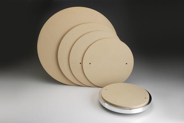 Four disc-shaped pottery templates and a metal turning wheel on a dark background, used for ceramic shaping and decorating.