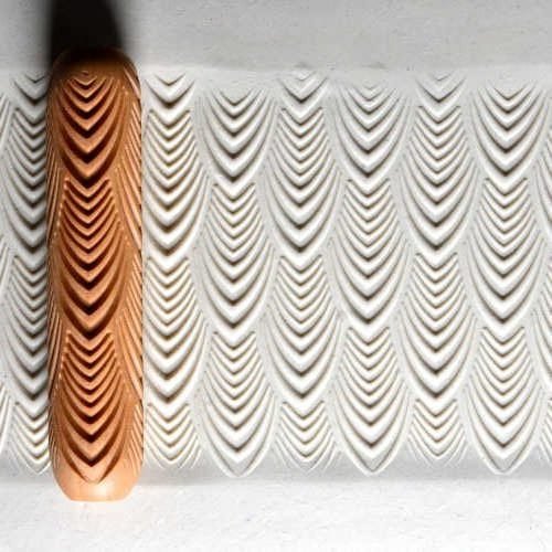 Patterned ceramic clay with textured waves, featuring an orange-brown clay roller and white unglazed surface for decoration.