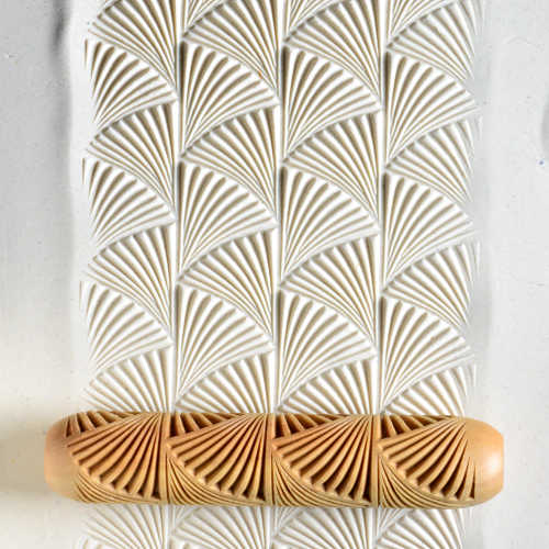 Textured white clay sheet with a carved roller tool featuring a spiral design, ideal for enhancing ceramics and pottery.