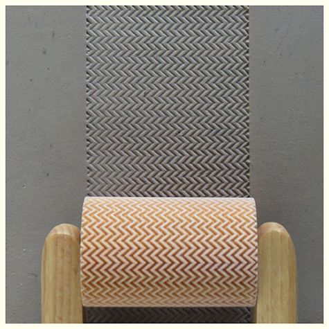 Ceramic texture rollers in gray and orange herringbone patterns, used for decorating clay surfaces in pottery.