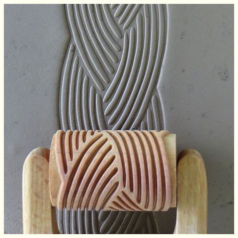 Clay texture roller imprinting a wavy pattern onto gray clay. Ideal for decorative ceramics and pottery applications.