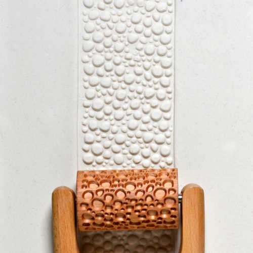 Textured white clay slab with bubble patterns, rolled with a wooden texture roller used for pottery and ceramic decoration.