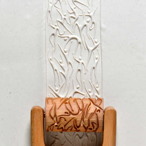 Rolled white clay with a textured pattern pressed by a wooden stamp, showcasing ceramic decorating techniques.