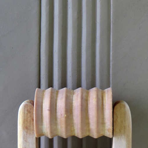 Clay slab with ribbed texture created by a rolling tool, ideal for pottery and decorative ceramic projects.