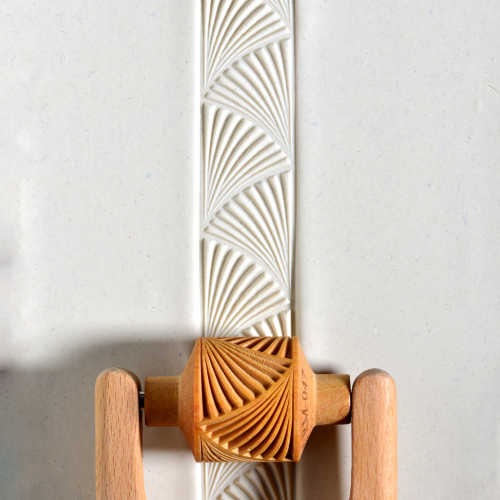 Ceramic texture roller impressing a carved pattern into raw clay, showcasing intricate design for artistry and decorating.