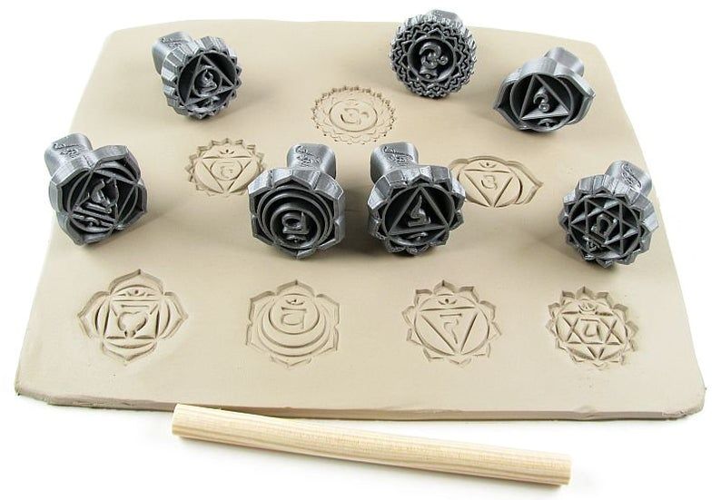Ceramic stamps showcasing chakra designs on a clay slab with a bamboo tool for decorating pottery.