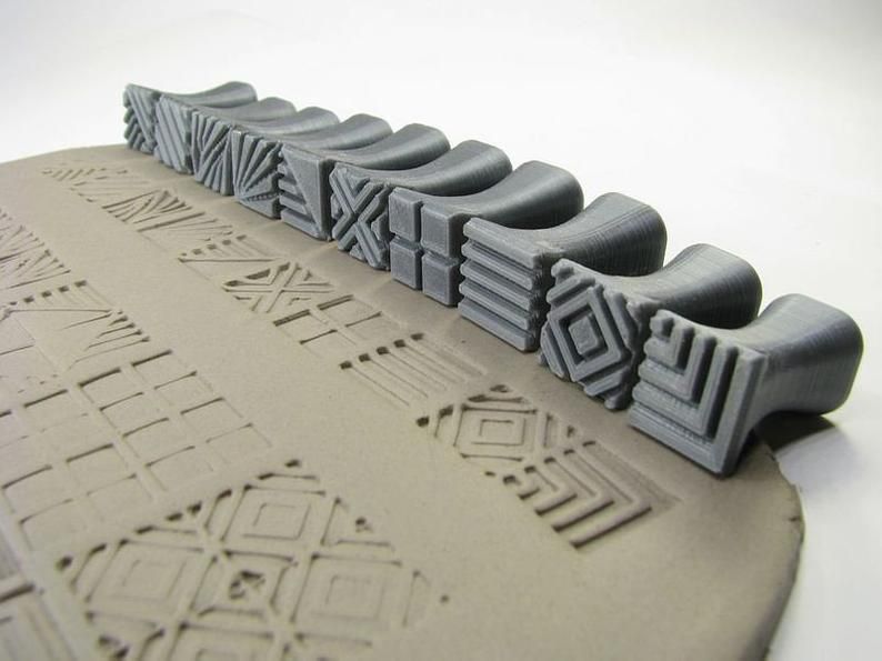 Gray pottery stamps arranged on a slab of clay, creating textured patterns for ceramic decoration and design.