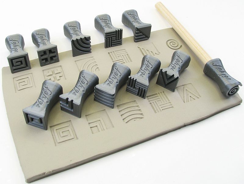 Set of ceramic texture tools on a clay slab, featuring various patterns and a wooden handle for imprinting designs.