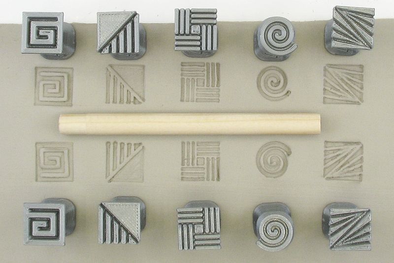Ceramic texture stamps arranged on clay with a wooden modeling tool for creating patterns in pottery projects.