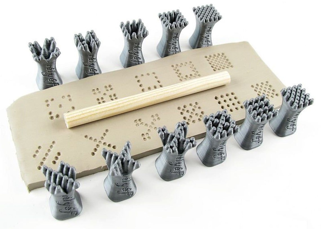 Set of textured clay stamps arranged around a slab of clay with a wooden dowel, used for decorating pottery at Georgies.
