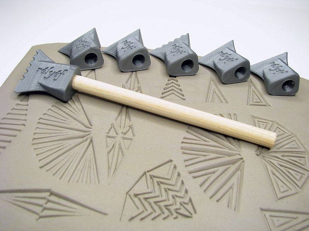 Ceramic pattern tools with wooden handle resting on textured clay, showcasing various stamped designs for pottery decoration.