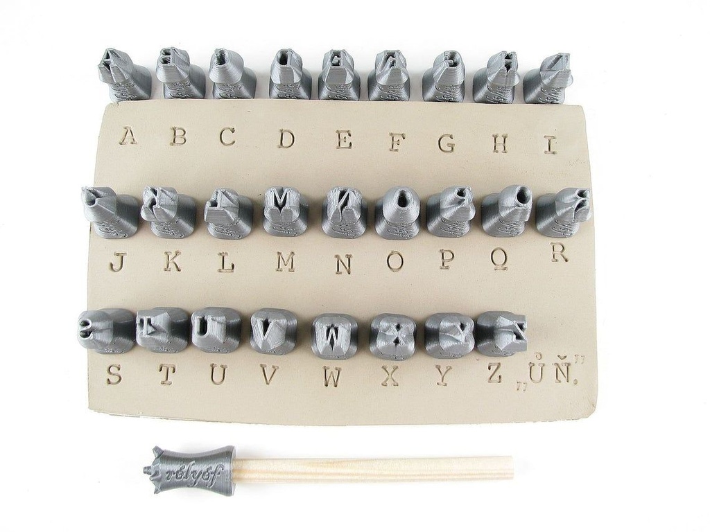 Clay alphabet stamp set displayed with letters carved into a clay slab, alongside a wooden handle for stamping.