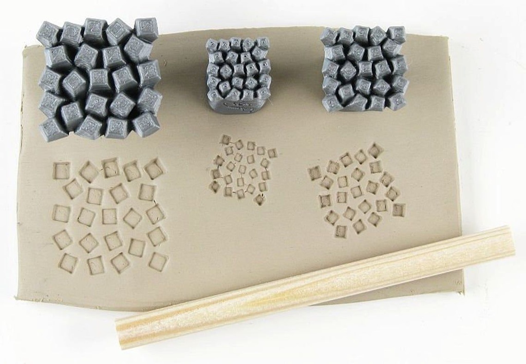 Gray clay stamps imprinting geometric patterns on a slab of beige clay, with a wooden tool for texture detailing.