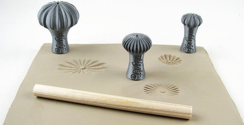 Three textured silicone stamps on clay with a wooden rolling pin, showcasing decorative techniques for pottery.