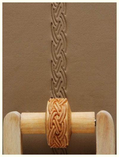 Ceramic textured roller creating a braided design on smooth clay, showcasing pottery decoration techniques.