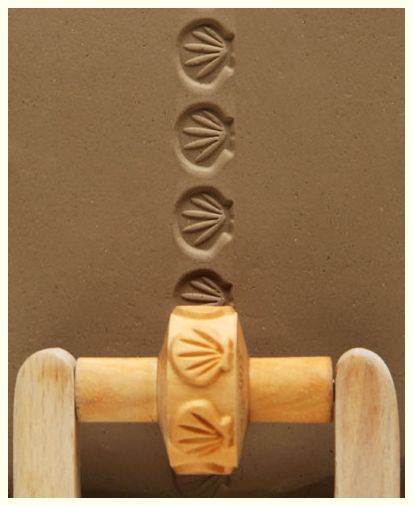 A rubber roller with a shell design imprints patterns onto a smooth clay surface, showcasing decorative pottery techniques.