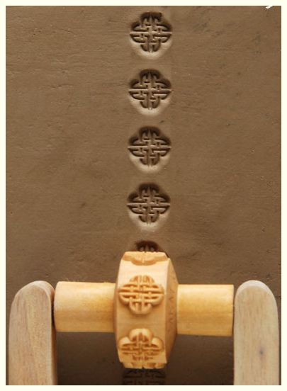 Textured clay slab with decorative stamped impressions using a ceramic roller tool, showcasing intricate patterns.