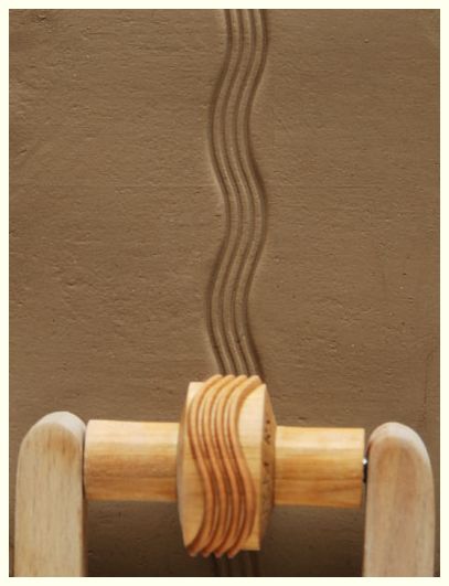 Clay tool with wooden handle creating wavy texture on moist clay surface in a pottery studio.