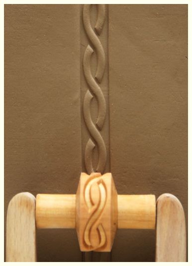 A close-up of textured clay showing a braided design made using a wooden stamp tool for pottery decoration.