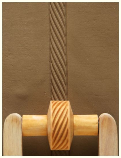 Wooden rib tool resting on textured clay surface with a twisted design, showcasing pottery design techniques.