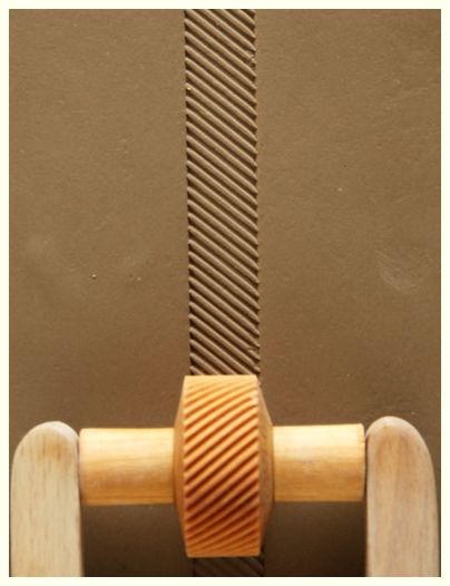 Close-up of a clay surface with a ribbed texture created by a wooden rolling tool, ideal for pottery decoration.
