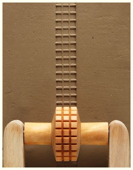 Wooden texture roller creating a grid pattern on brown clay, showcasing pottery decorating techniques and ceramic tool use.
