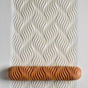 Textured white clay surface with wavy patterns, alongside a patterned clay roller tool in terracotta.