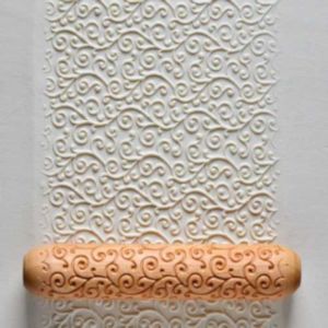 A decorative ceramic rolling pin rests on a textured clay surface, featuring intricate swirl patterns.