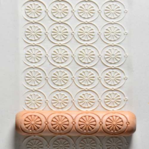 Textured clay mat with floral patterns rolled by a wooden stamping tool, ideal for ceramic decorating and surface design.