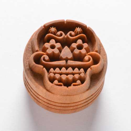 Carved clay texture stamp featuring a decorative skull design with floral motifs, ideal for pottery decoration.