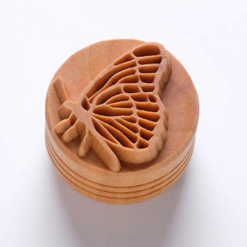Butterfly-shaped ceramic texture stamp on a circular wooden base, used for decorating pottery and clay projects.