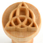 Detail of a carved wooden pottery stamp featuring a triad design, used for decorating clay and ceramics in studio work.