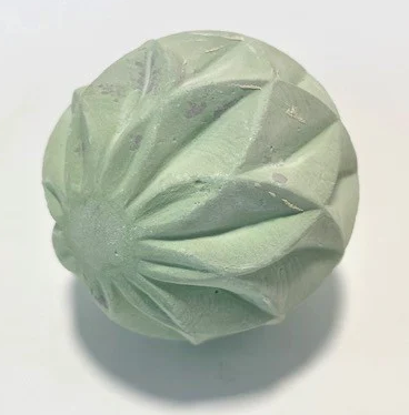 Green ceramic sphere with textured, petal-like design, showcasing a sculpting technique suitable for pottery and casting projects.