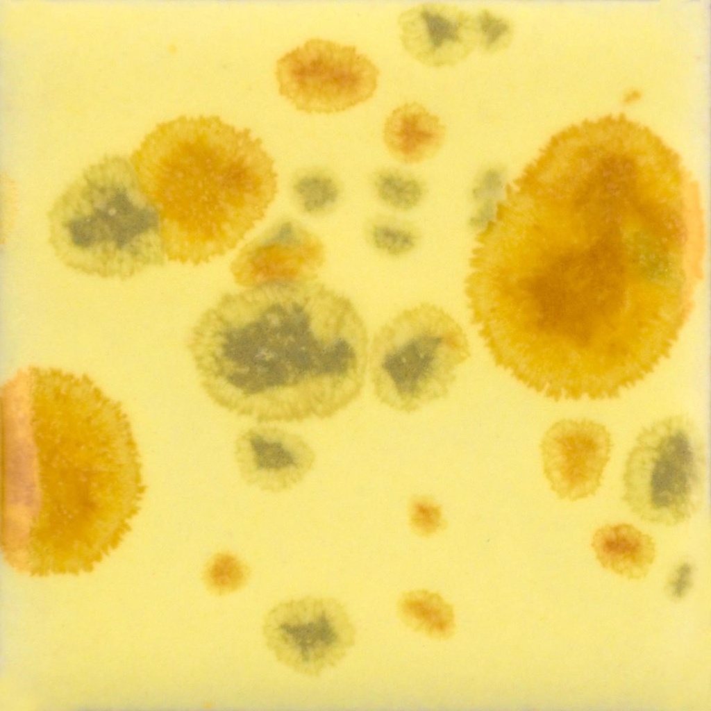 Yellow glaze sample with irregular spots in orange and green, showcasing unique decoration techniques for ceramics.