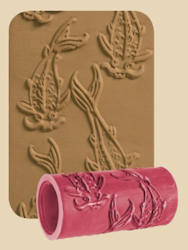 Textured clay plate with fish design and a pink clay roller tool used for pottery decoration.