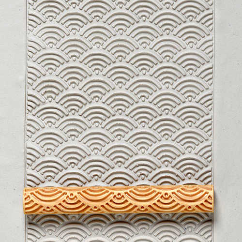 Textured white clay slab with wave pattern impression and an orange clay roller stamp, showcasing ceramic decoration techniques.