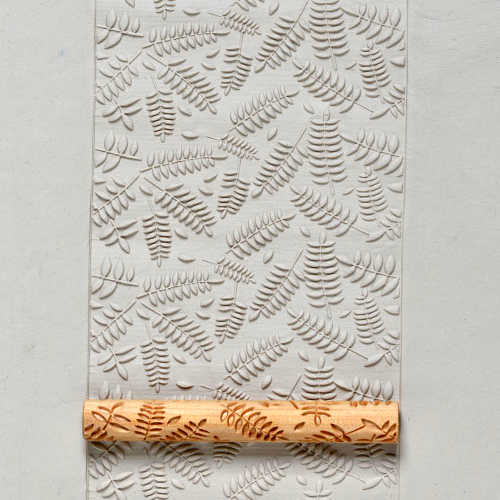 Embossed ceramic slab featuring fern patterns with a textured bamboo rolling tool for clay decoration.