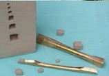 Two ceramic carving tools rest beside sculpting clay with textured surfaces, featuring small clay pieces on a blue background.