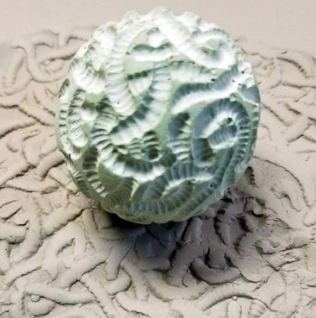 Textured green clay sphere on a sandy surface, showcasing intricate patterns for ceramic decoration and sculpting techniques.