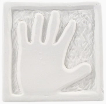 Handprint impression in white clay, framed with textured background; a sculpture technique for creating keepsake pieces.