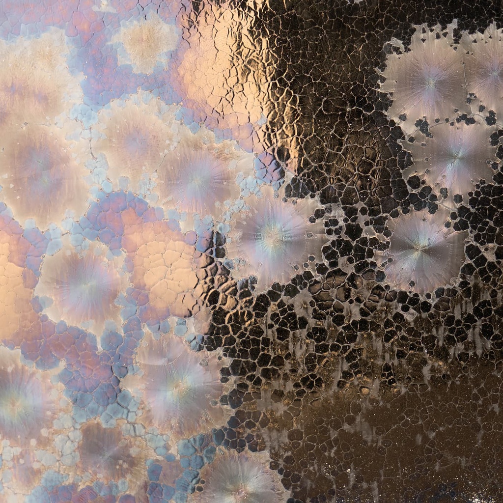 Textured ceramic glaze with iridescent flowers in soft pastel colors on a dark background, showcasing unique surface effects.
