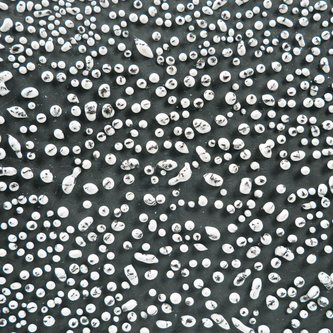 Various sizes of white ceramic beads scattered on a dark background, showcasing textures for pottery decoration.