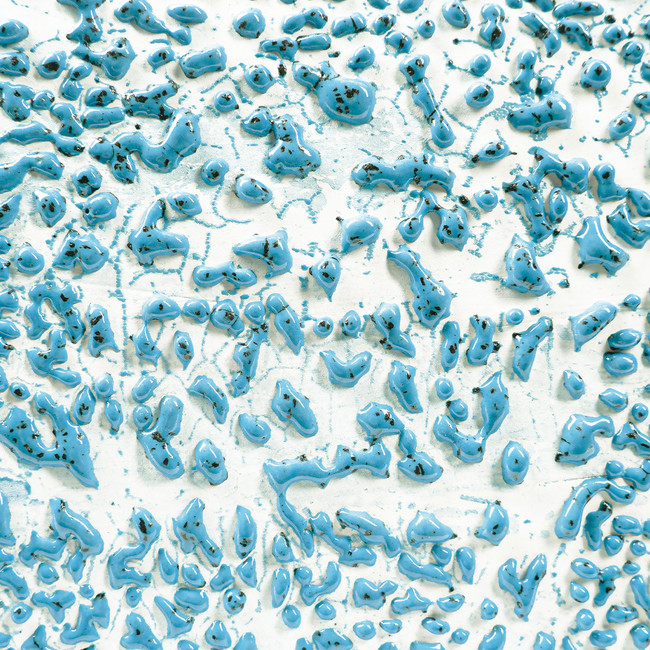 Textured surface of blue glaze with glossy droplets on white clay, showcasing layering and variation in ceramic craftsmanship.
