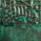 Textured green ceramic glaze with intricate patterns and varied surface techniques applied on clay for decoration.