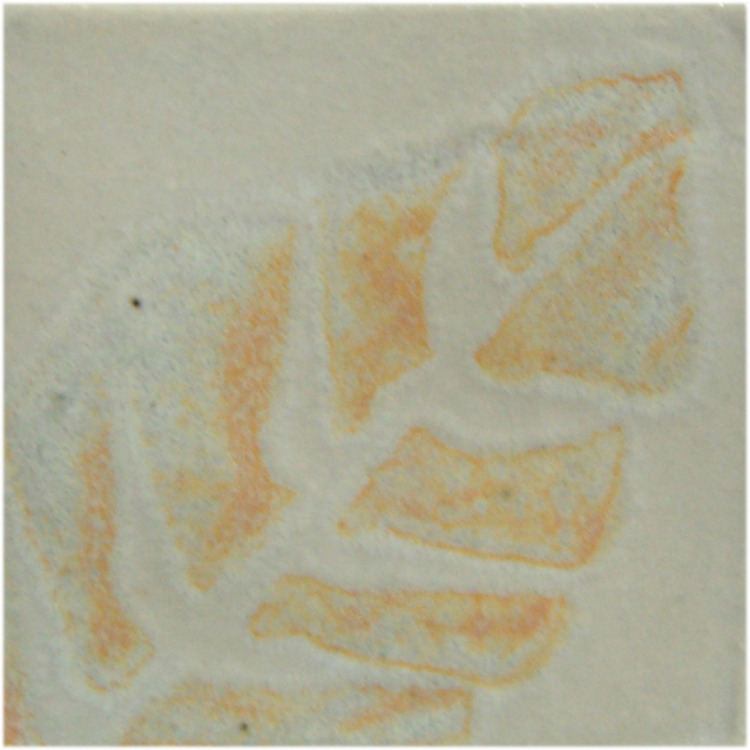 Close-up of a textured clay tile with a leaf imprint, featuring soft orange and white glazes typical of ceramic decoration techniques.